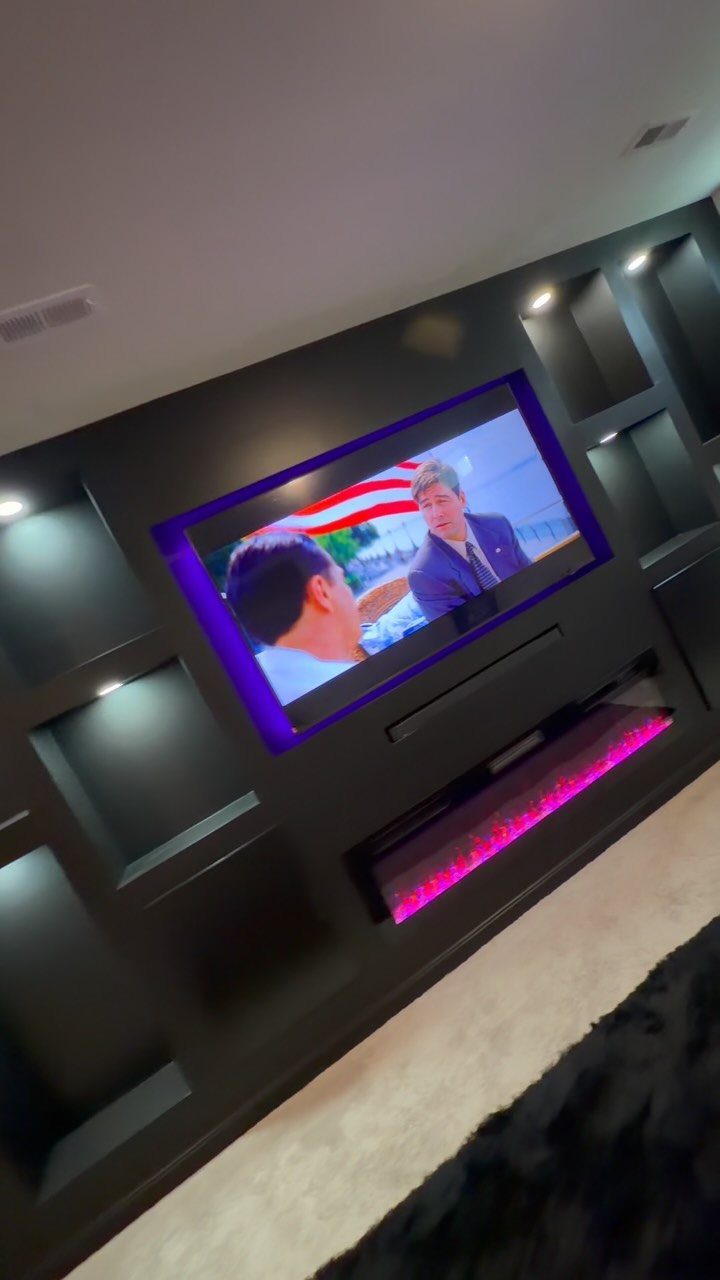 A dark built-in entertainment wall unit with recessed shelving and purple ambient lighting.