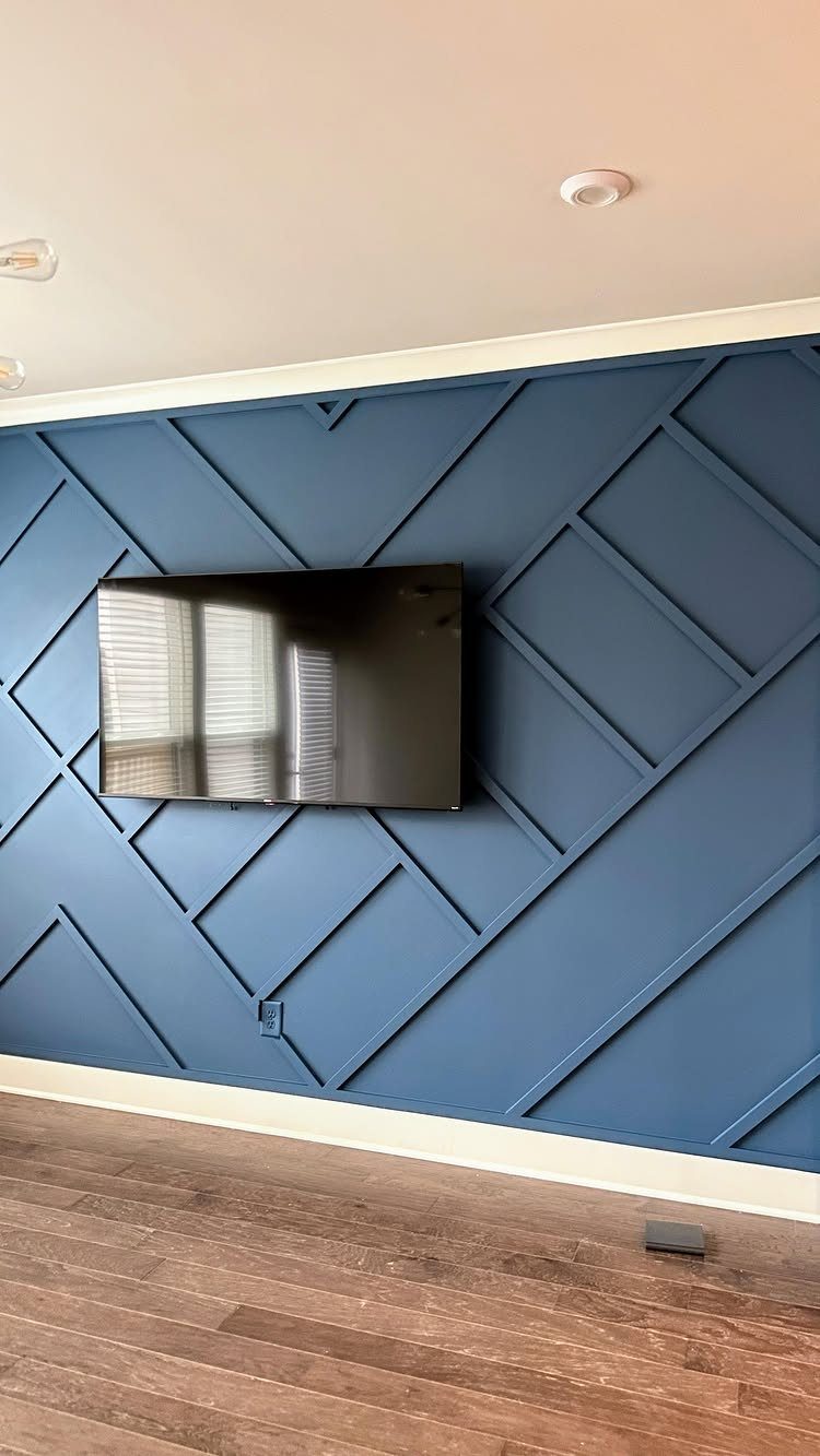 Blue geometric patterned accent wall with a mounted television above wooden flooring.