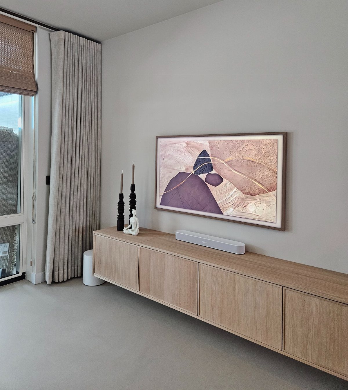 A long light wood floating console sits below framed abstract art on a neutral wall.