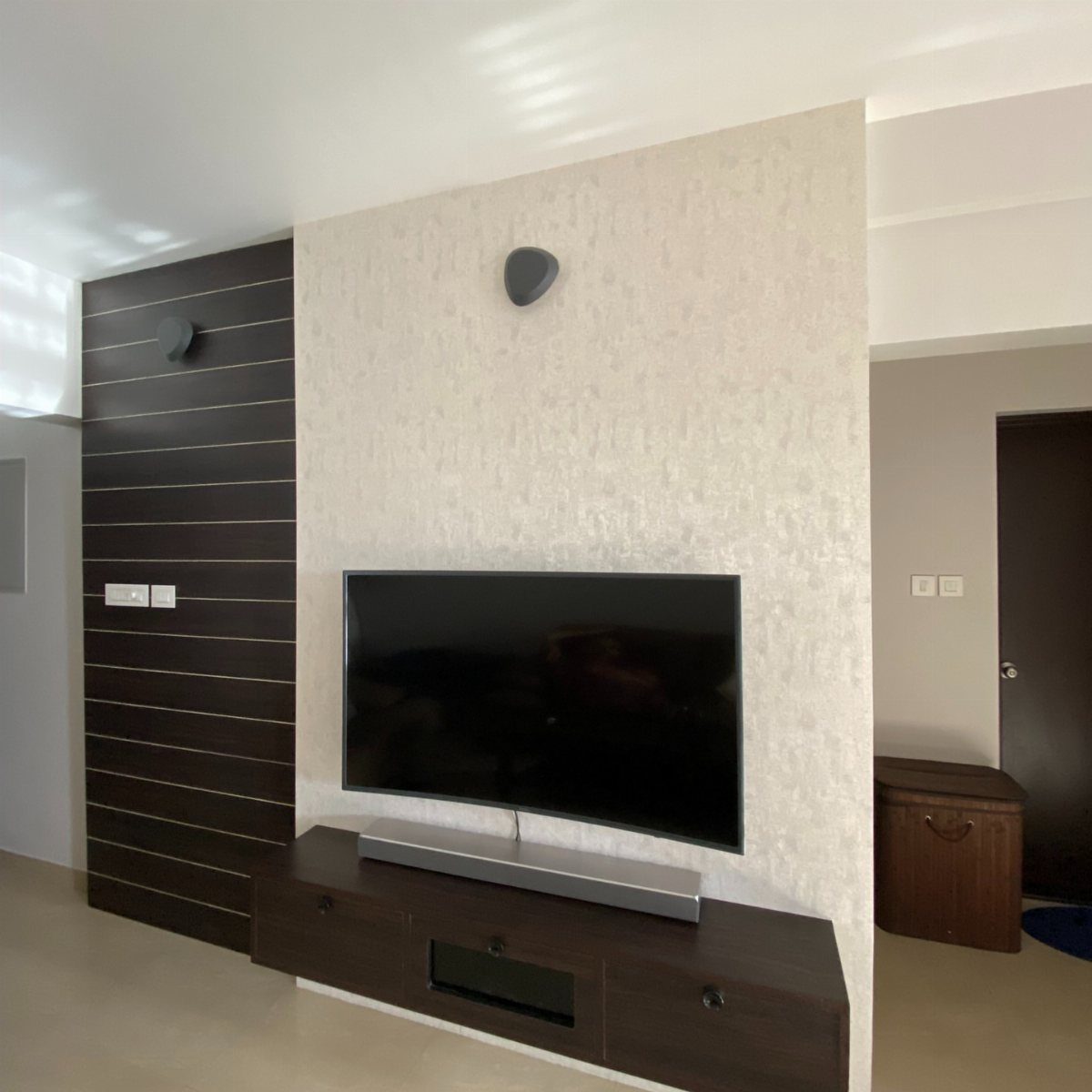 Television mounted on a textured white wallpapered wall panel next to dark wood paneling.