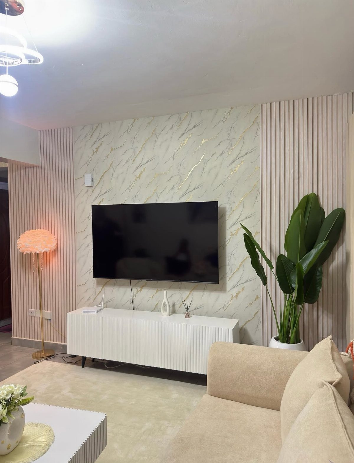 Television mounted on a marble patterned wallpaper panel with vertical wooden slats and white console.