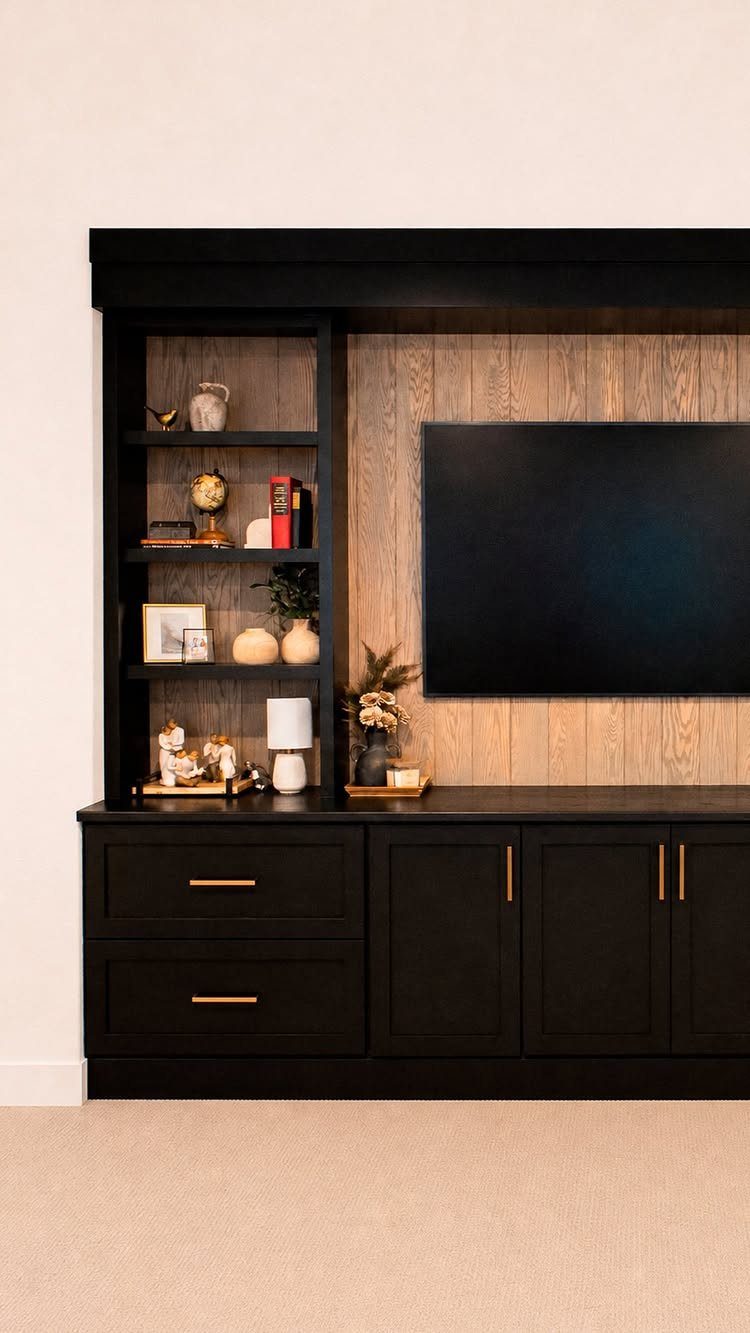 Black built-in wall unit with open shelving, a television, and lower storage cabinets against wood paneling.