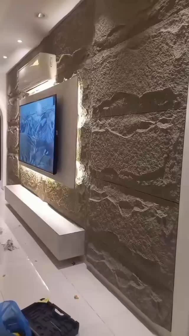 Textured stone wall panels with a mounted television and a long white floating console below.