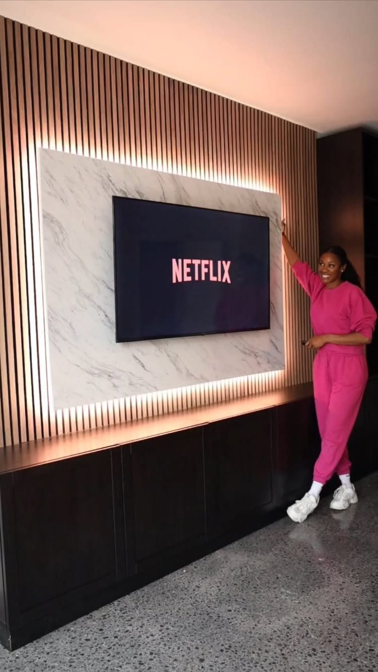 A television mounted on a marble panel surrounded by vertical wood slats with integrated LED lighting.