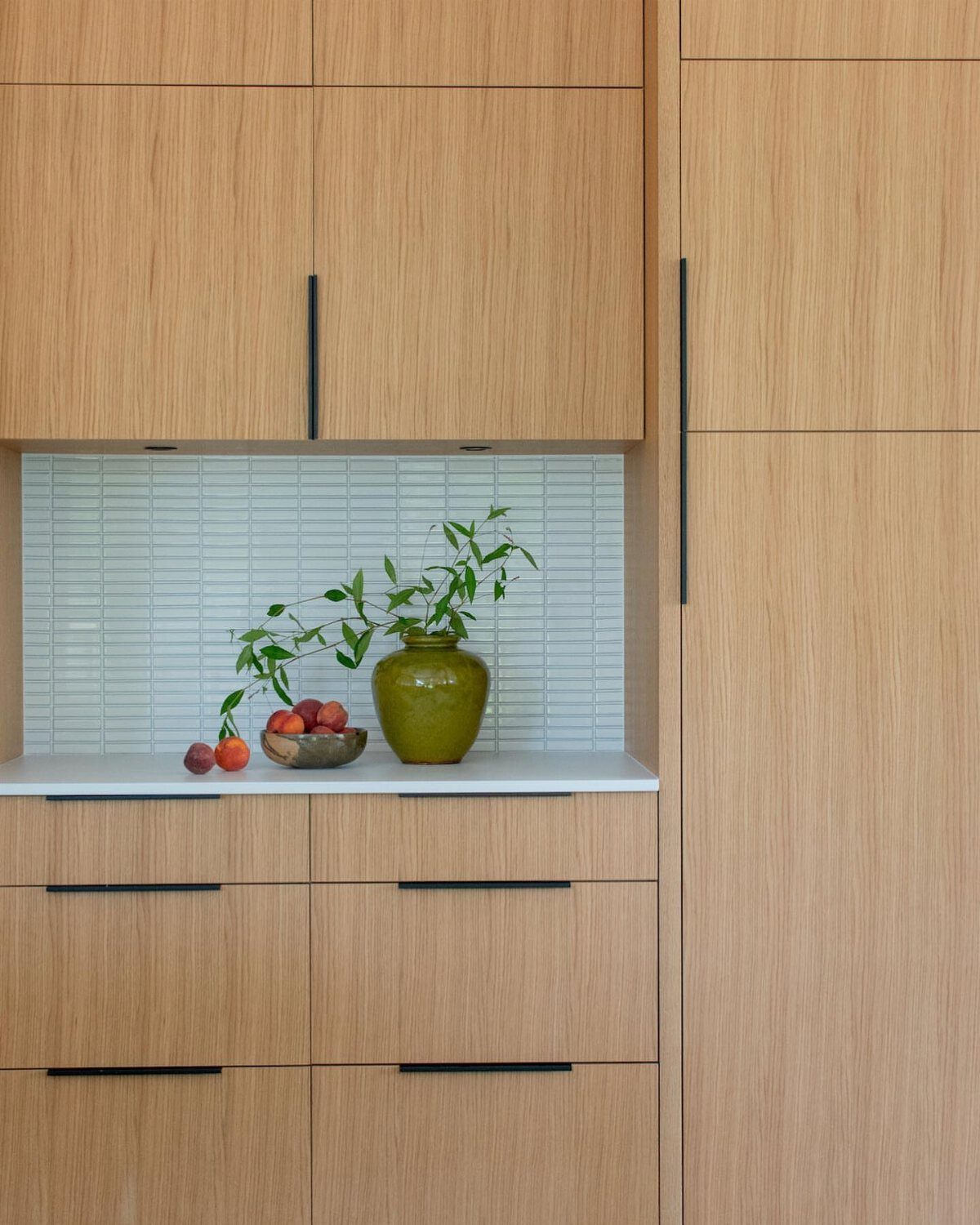 Light wood flat-panel kitchen cabinets with black handles and a white countertop.