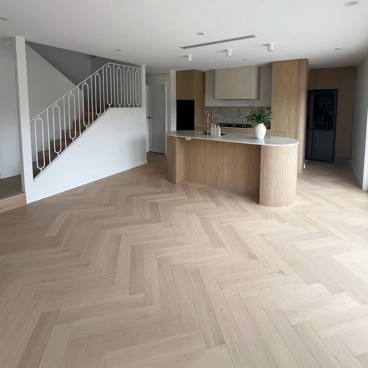 Light white oak floors in a herringbone pattern within a modern kitchen and living space.