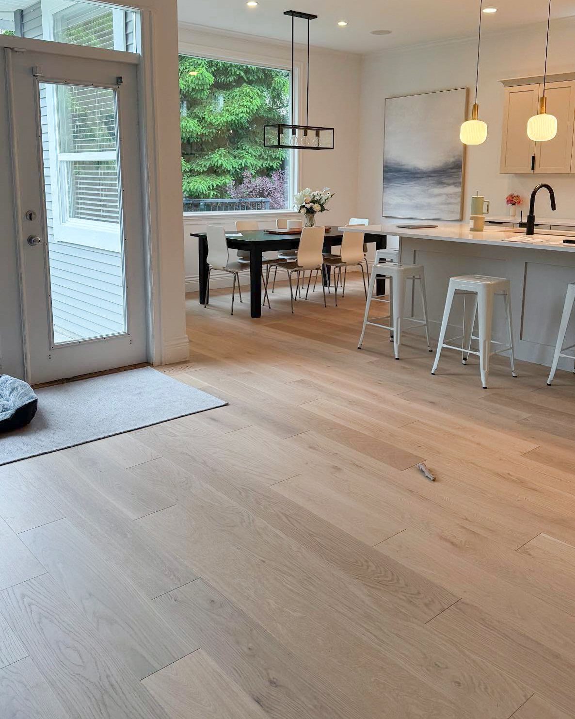 Light white oak wood flooring extends through a bright, modern kitchen and dining area.