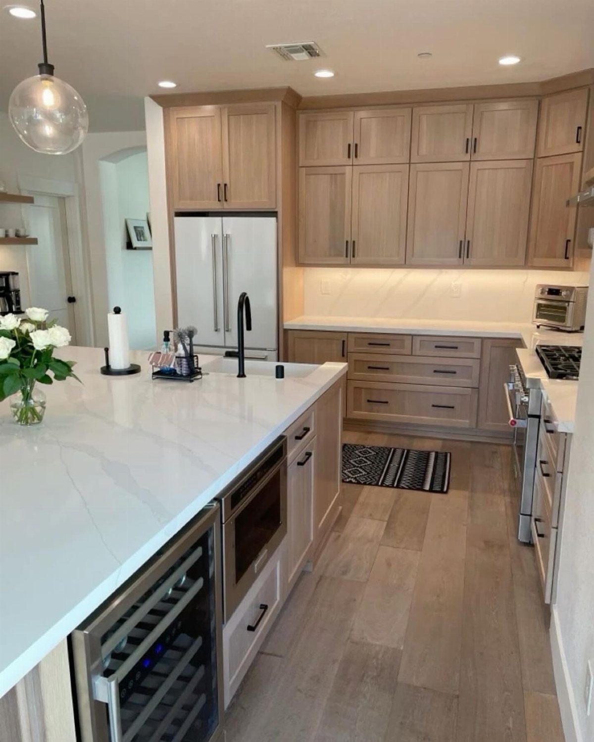 Light natural wood cabinets and white countertops in a modern, bright kitchen setting.
