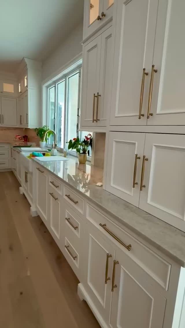 White kitchen cabinets with gold handles and light wood flooring under a bright window.