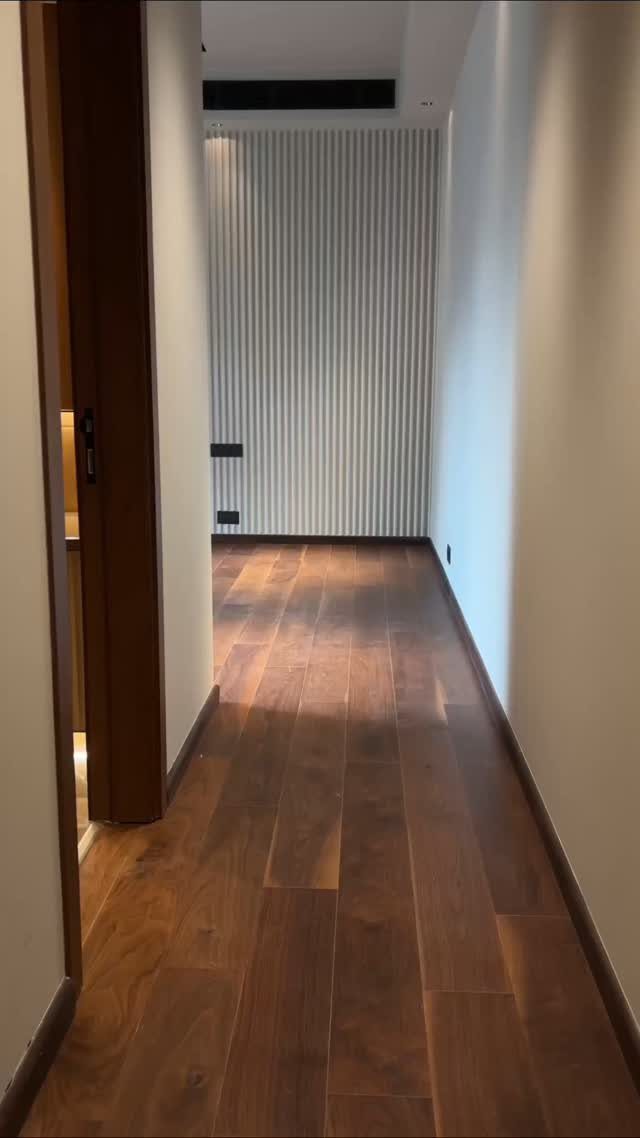 Dark brown wood plank flooring stretching through a long, brightly lit hallway with white walls.