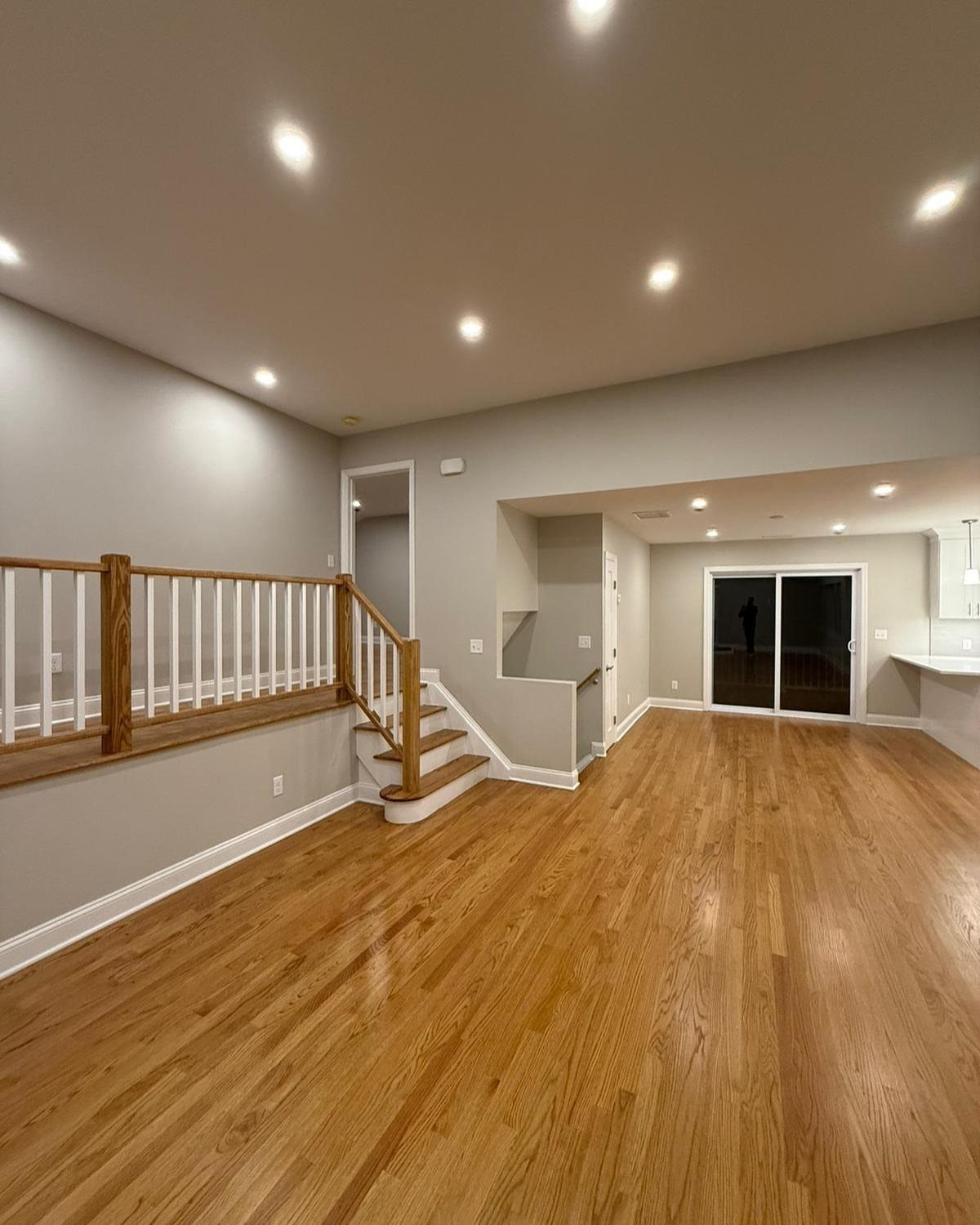 Golden oak wood flooring in a large room with gray walls and a staircase.