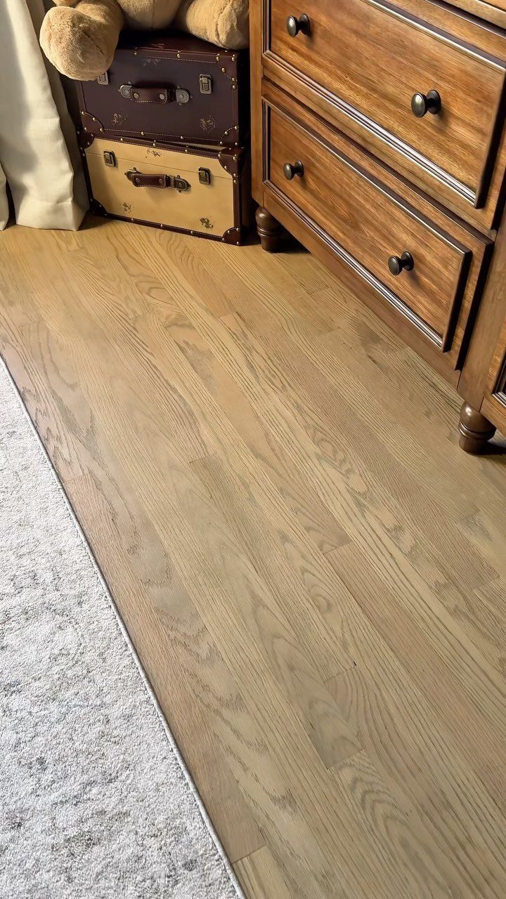 Light oak wood flooring next to a wooden dresser and vintage suitcases in a room.