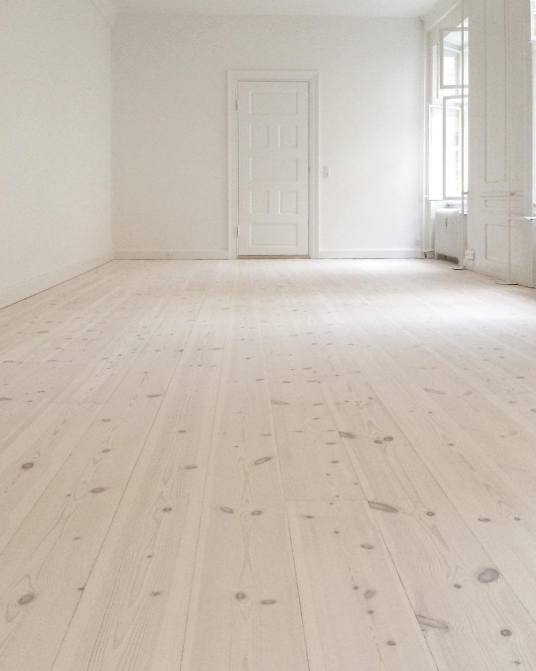 Light whitewashed wood plank flooring in a bright, empty white room with a door.